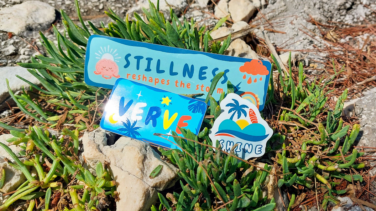 Three colorful decorative stickers among green succulent plants and small rocks outdoors with bright blue backgrounds and tropical, abstract illustrations.